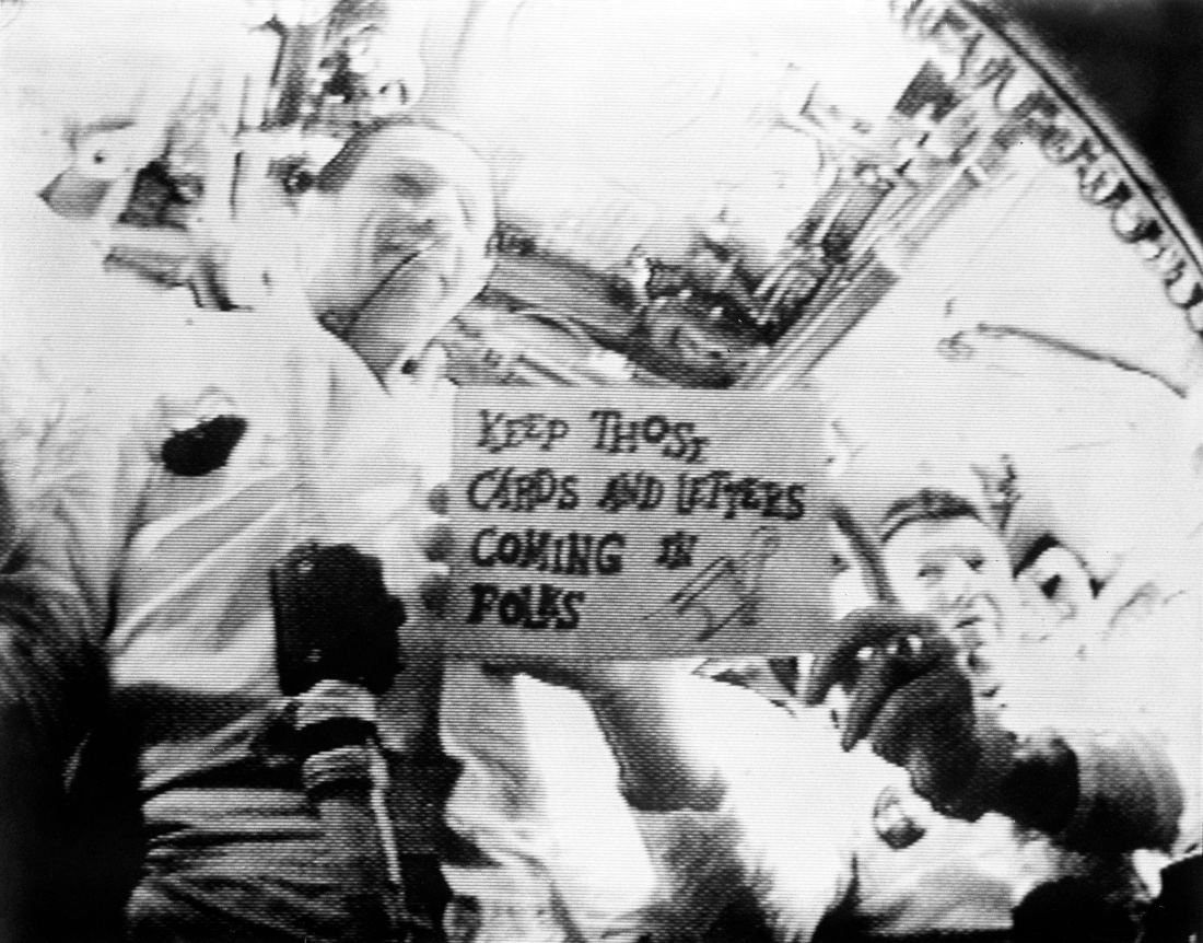 image of apollo astronauts on television holding a small sign that reads keep those cards and letters coming in folks