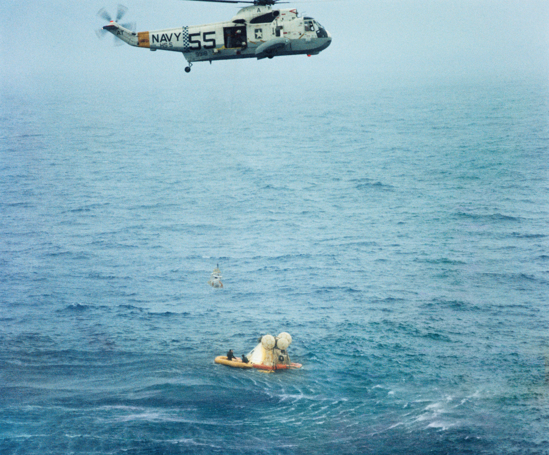 image of a helicopter lowering a harness down to Apollo 7 Command Module and astronauts floating in the Atlantic ocean